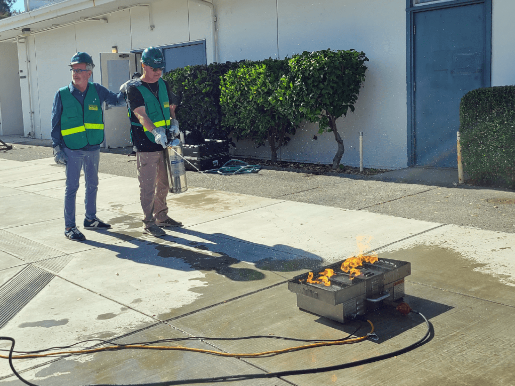 Two CERT volunteers practice with a fire extinguisher on a small fire.